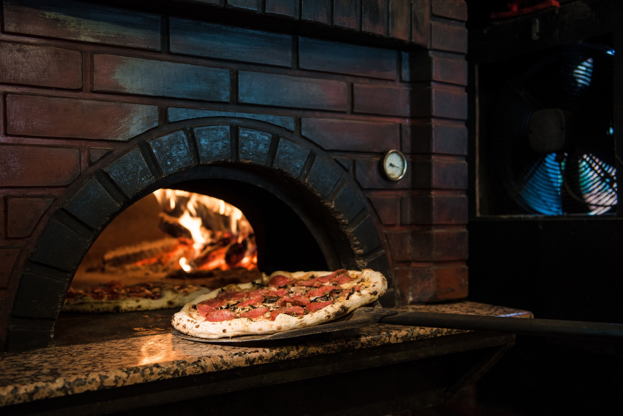 close up view of cooking process of raw pizza on wooden stove in brick oven