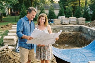 Couple de propriétaires examinant les plans techniques d'une piscine familiale en cours de construction dans leur jardin